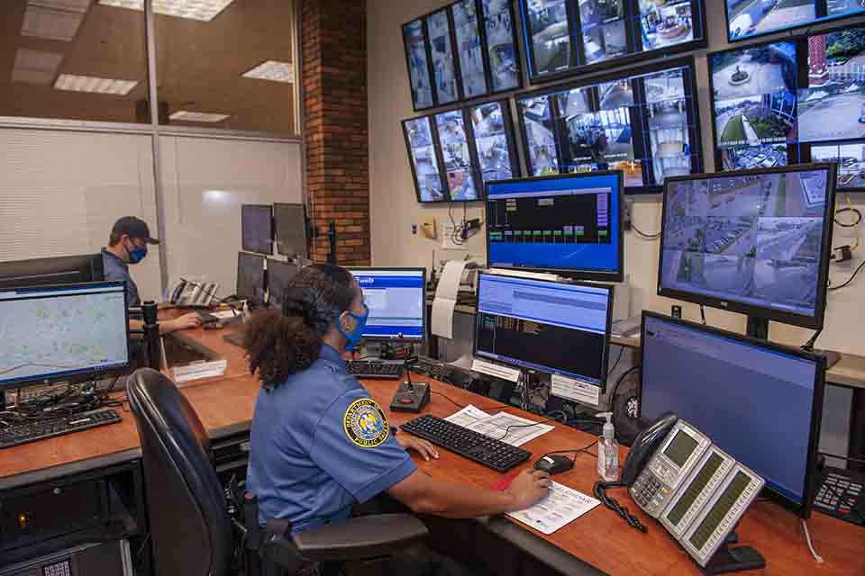 DPS officer sits in front of a bank of monitors and screens.