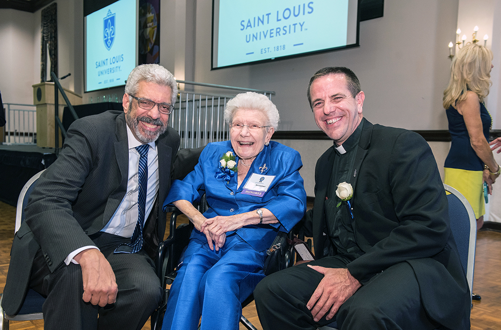 Mary Bruemmer seated with SLU President Fred Pestello and Father Chris Collins after a ceremony