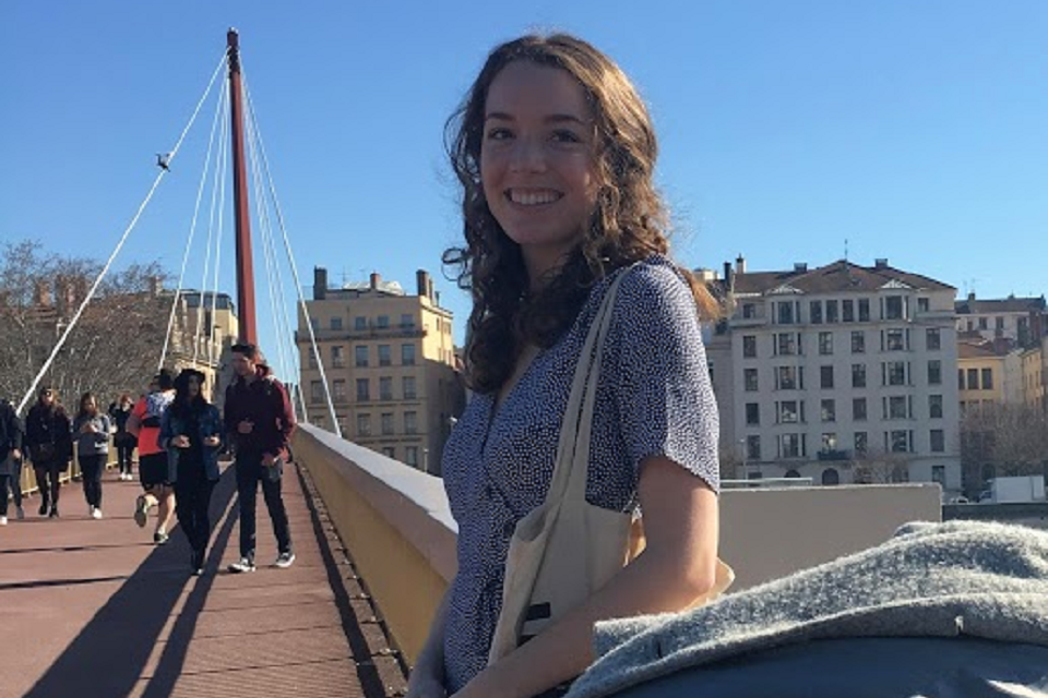 Rachel Fox stands on a bridge in a city with other people walking by.