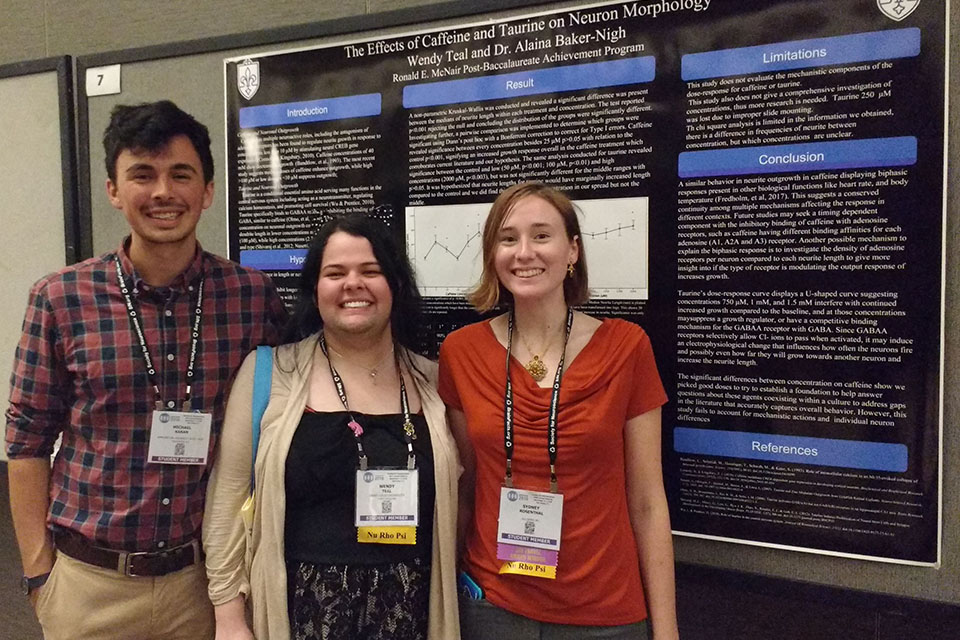Three students wearing conference lanyards stand in front of a conference poster that reads "The Effects of Caffeine and Taurine on Neuron Morphology"