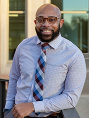 A bearded African American man wearing a blue shirt and tie.