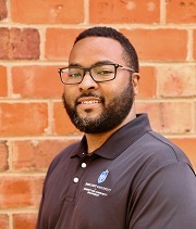 Michael Hankins, headshot, wears a SLU polo shirt and smiles, standing in front of a brick wall.