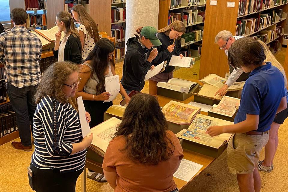 Students and faculty members examine books and other materials around tables and shelves in the library.