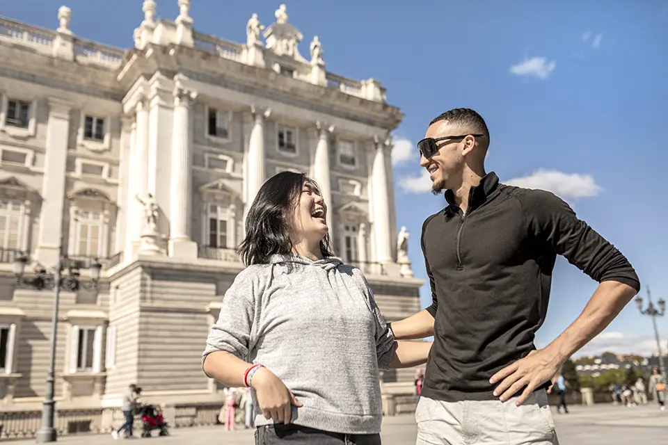 Two students laughing and strolling near the Royal Palace in Madrid.