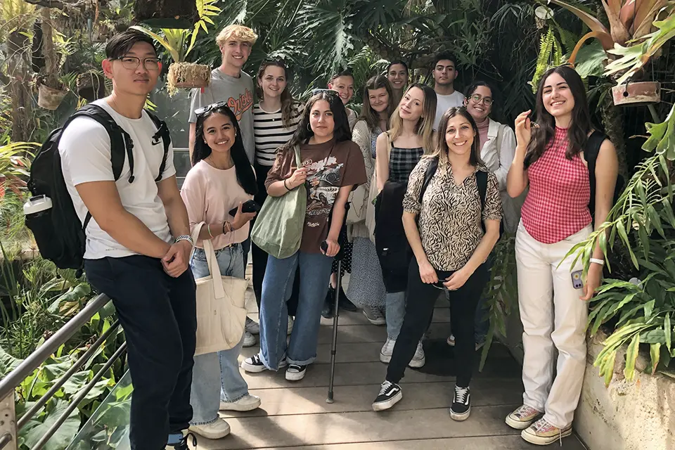 Students and professor stand on a walkway surrounded by lush plants.