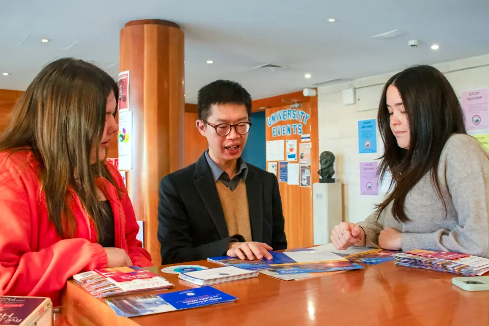 3 people consult information brochures in a building lobby.
