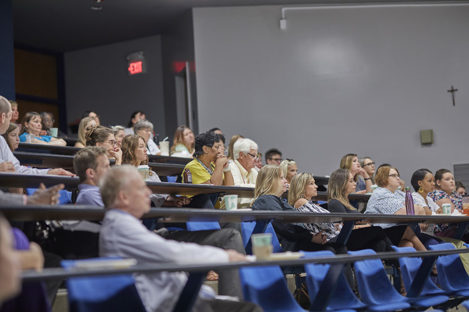 Students and faculty members sit at seats in lecture auditorium.