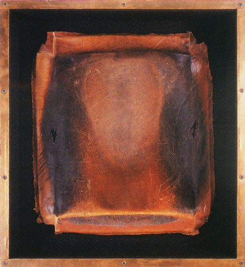 An artwork by Daniel Goldstein titled Icarian XI / Leg Extension. Inside a square-shaped case with a brass border, a leather workout bench cover is mounted. The surface of the leather is worn, and stained and darkened in a way that suggests the silhouette of a human head.