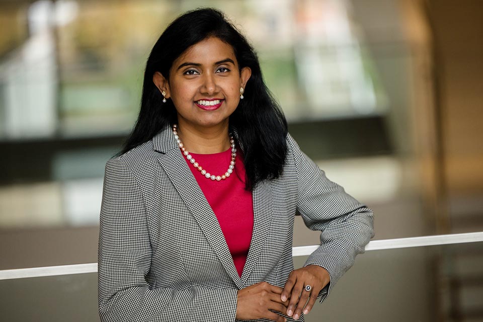 Portrait of Farzana Hoque wearing a business suit and leaning against a railing.