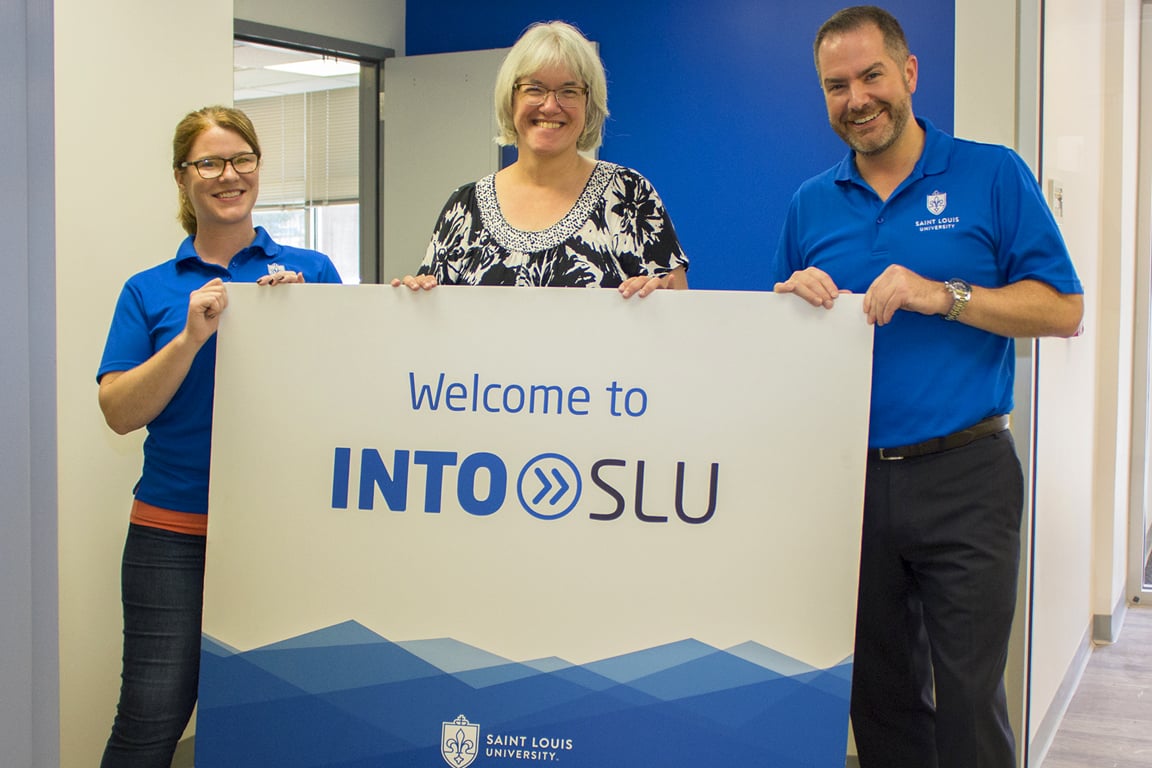Annie Rosenkranz, director of student experience, Anneke Bart, Ph.D., academic director, and Tim Hercules, J.D., M.I.B., executive director of INTO Saint Louis University, pose at the front desk of the new space in Beracha Hall.