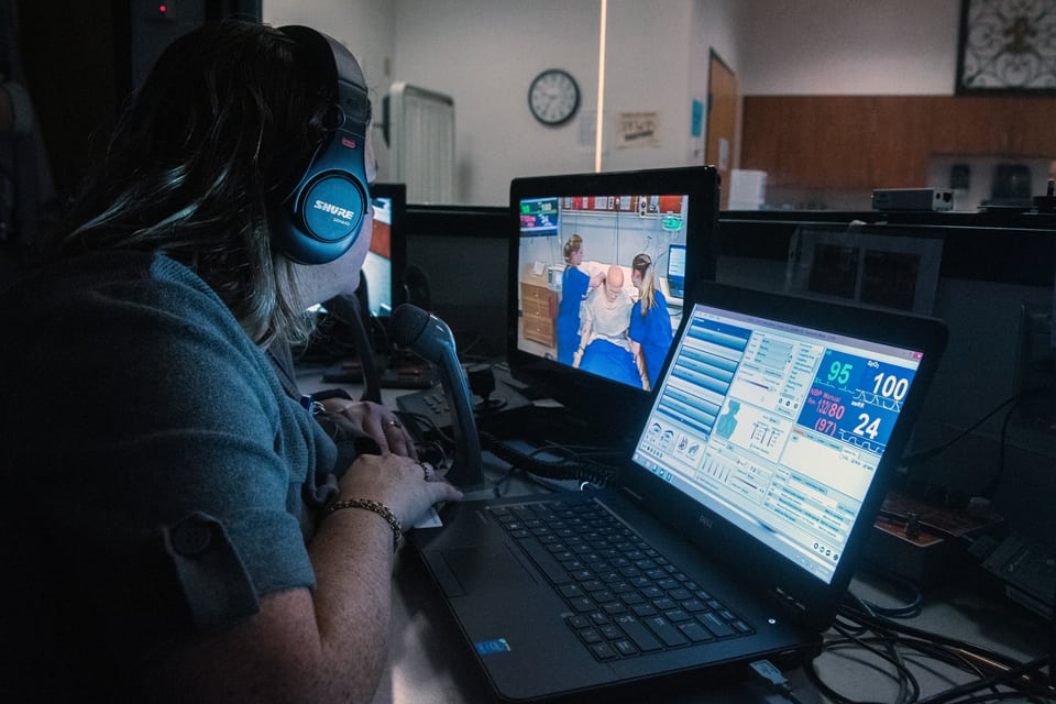 SLU Nursing student with headphones works reviews video on monitor of mock nursing proceedure