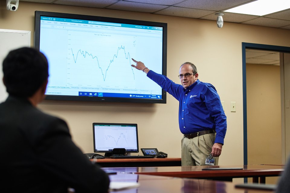 Michael Elliott, Ph.D., stands in the front of a conference room in a meeting, pointing at a screen with grahpical data.