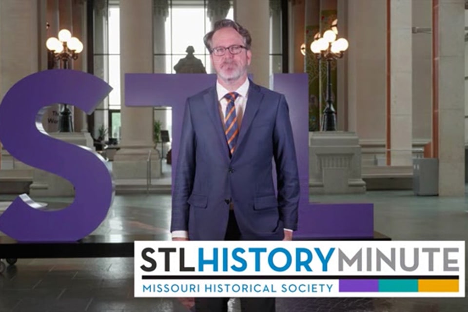 Sowell stands in front of a large "STL" sculpture at the Missouri History Museum. Text overlays reading "STL History Minute, Missouri Historical Society""