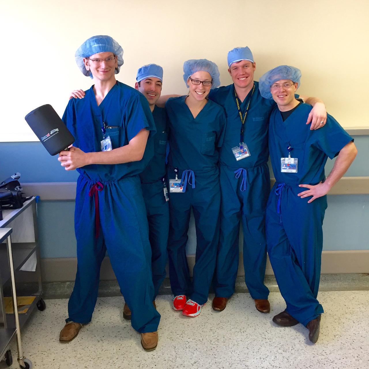 Five orthopedic surgery residents wearing surgical scrubs pose for a picture