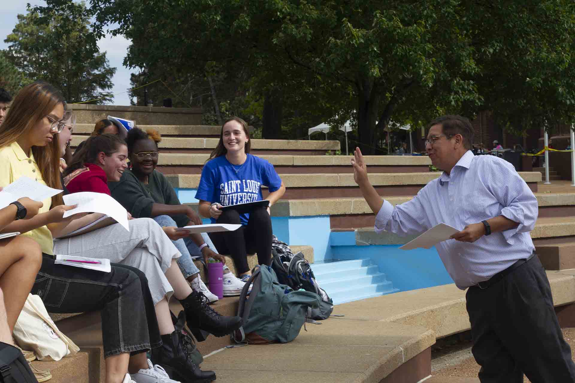 A professor leads a discussion while students sit near one of SLU's many fountains.