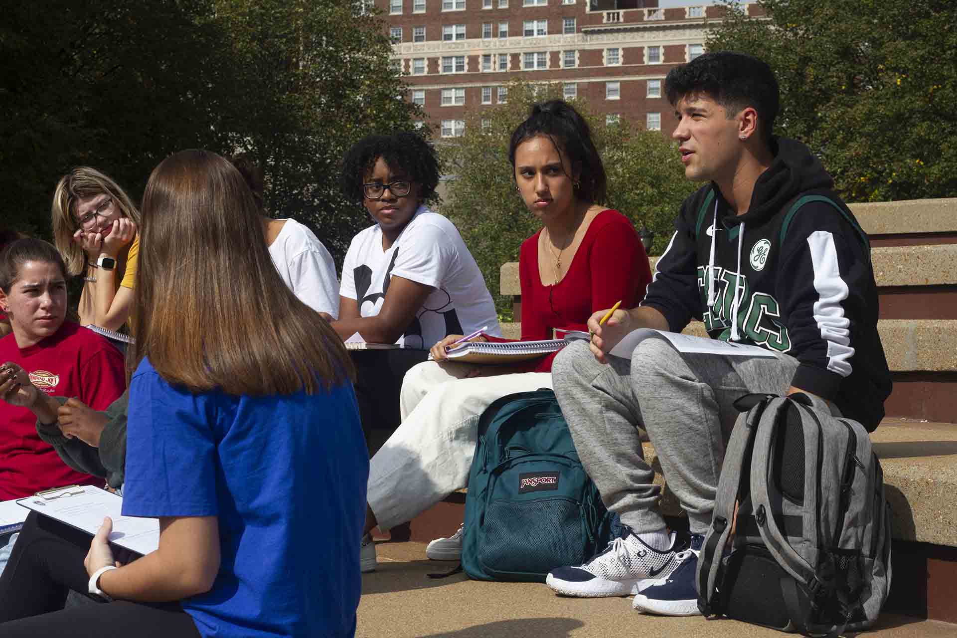 Students engage in class discussion while sitting outside on a sunny day.