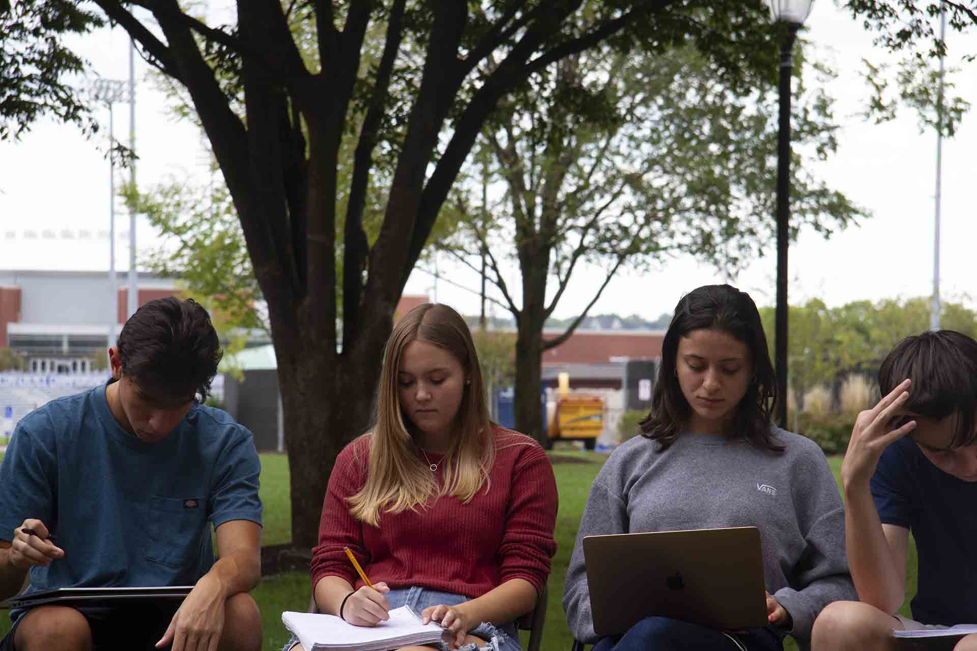 Students take notes during an outdoor class discussion.