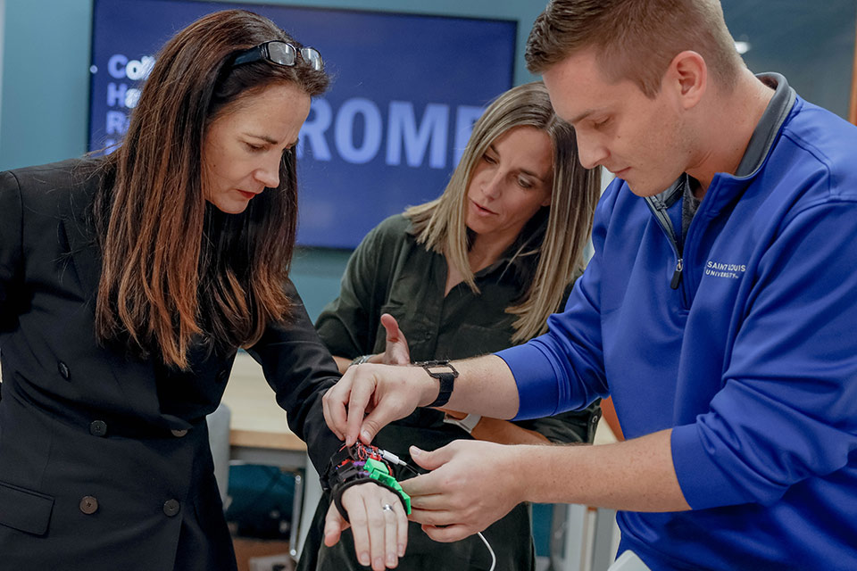 U.S. Director of National Intelligence Avril Haines, left, is fitted with a haptic wearable device by Bryan MacGavin, right, as CHROME Lab director Jenna Gorlewicz, Ph.D., looks on during a tour of the ISE Building in connection with a recently announced grant SLU received from the Office of the Director of National Intelligence. Photo by Sarah Conroy,