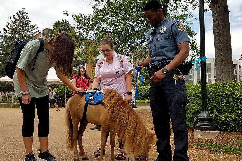 Officer Joshua Johnson (right) helps students chill-out during exams by escorting a therapeutic mini-horse around campus to visit them.