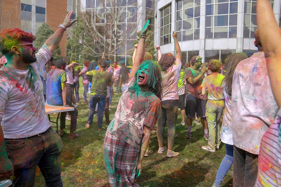 A photo of students raising their hands and covered in bright-colored powder called gulal during a recent campus celebration of Holi, a Hindu festival of colors. 
