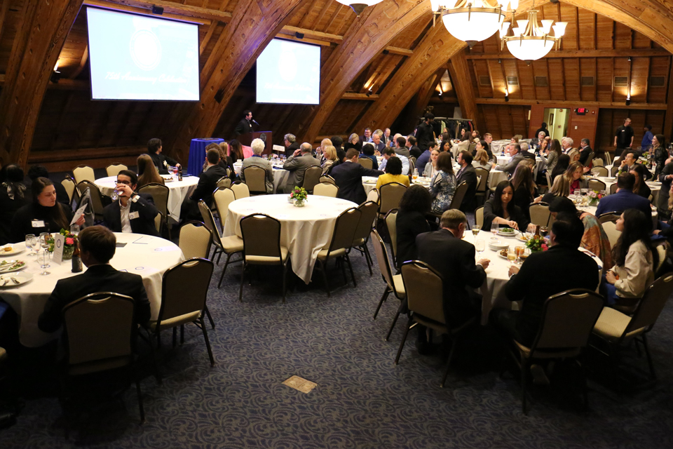 Event participants sit at tables and listen to a speaker at the lectern.