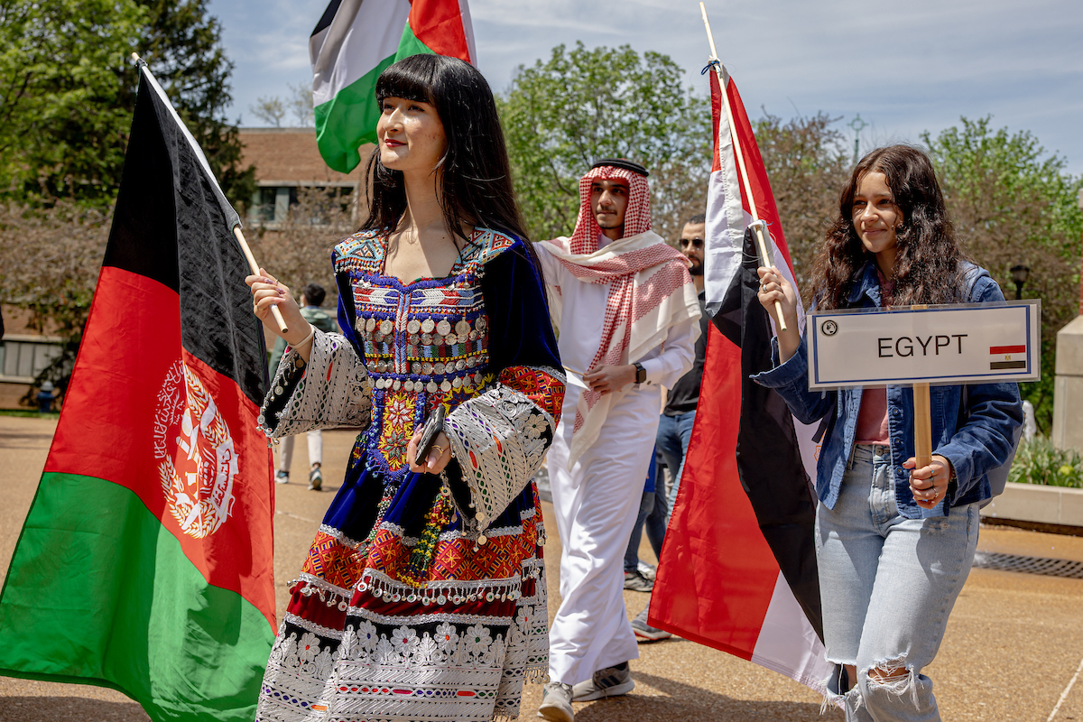 Slide 4: A student wearing traditional dress carries the flag of Afghanistan, followed by a student carrying the Egyptian flag.