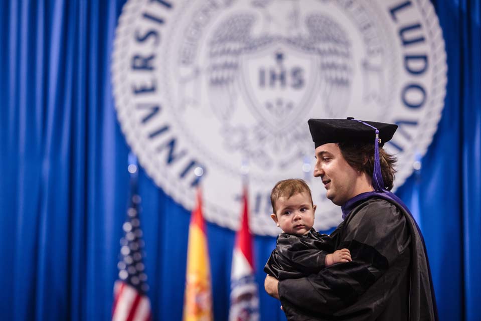 A graduate of the School of Law crosses the stage with his baby during the recommencement at Chaifetz Arena on May 18, 2023. Photo by Sarah Conroy.