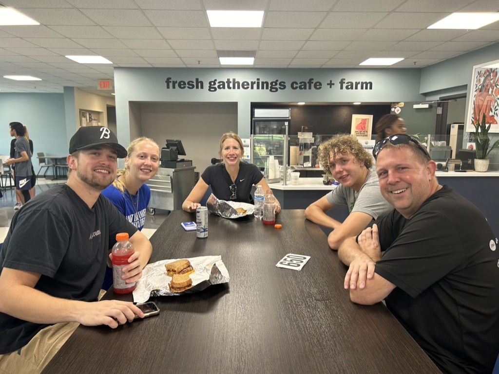 A family of five sits at a table together in Fresh Gatherings. 