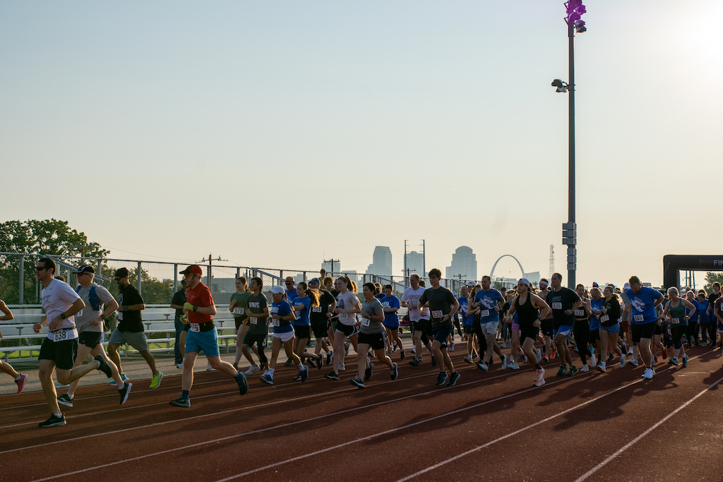 A group of people running on a track with the St. Louis skyline behind them.
