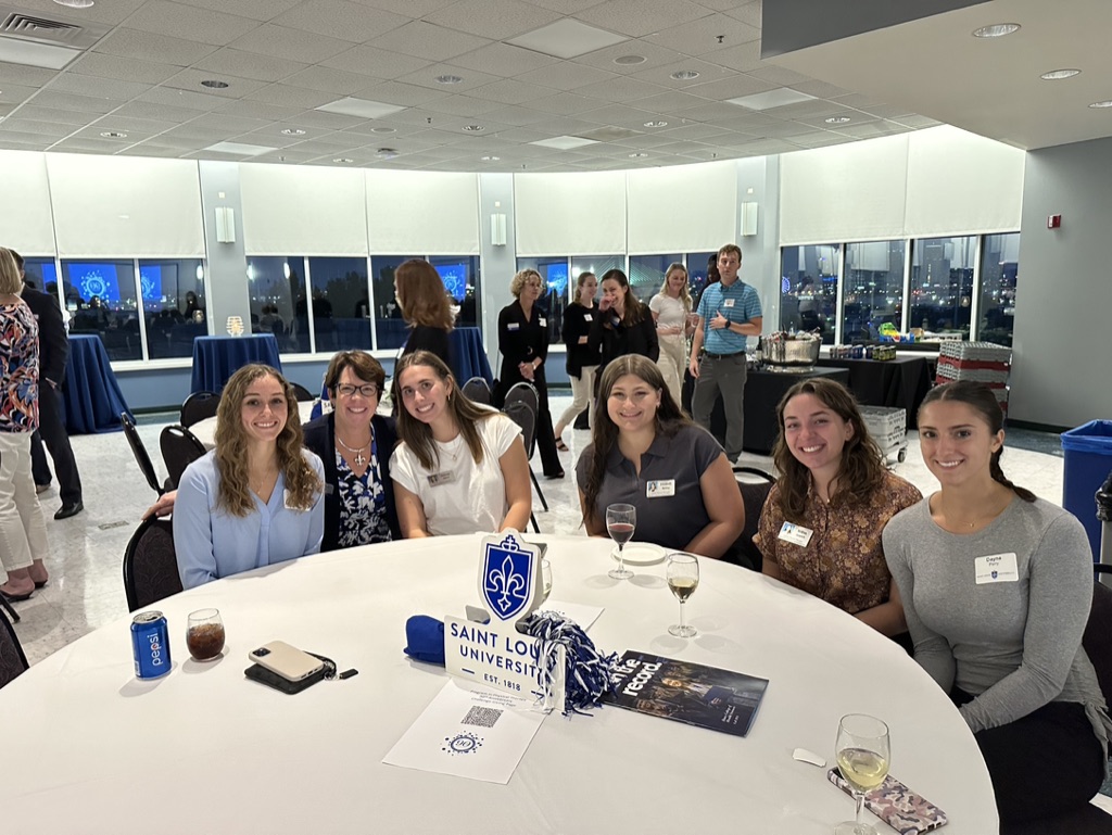 Five students and one faculty member sit around a table at the Program in PT's 90th anniversary dinner. 