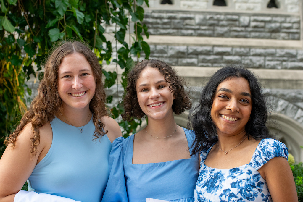 Three girls wearing blue and white dresses stand outside college church together. 