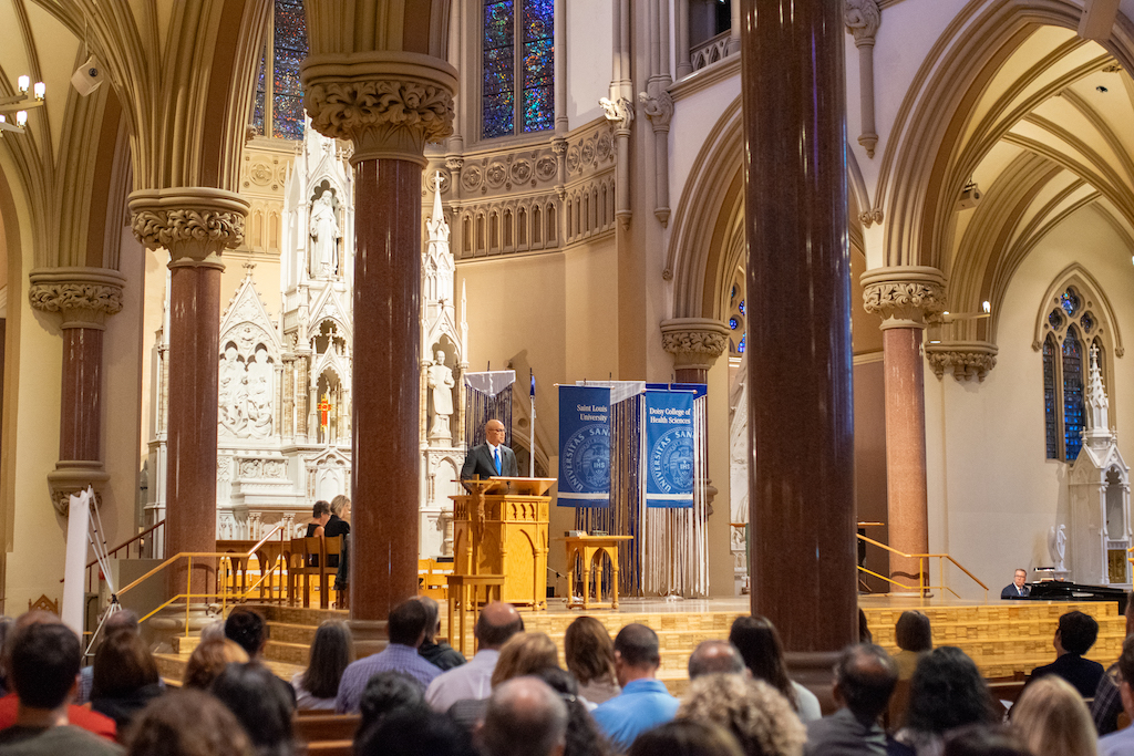 Dr. Rousseau stands at the front of college church behind the podium. 