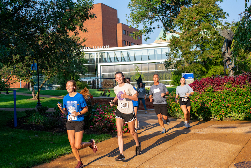 Four people running in the courtyard between the Education Union and the Allied Health Building. 