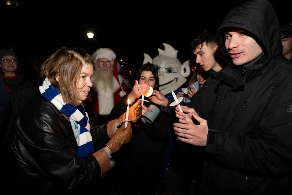 First Lady Fran Pestello, Ph.D., shares a candle with students at Christmas on the Quad. Photo by Luke Yamnitz.