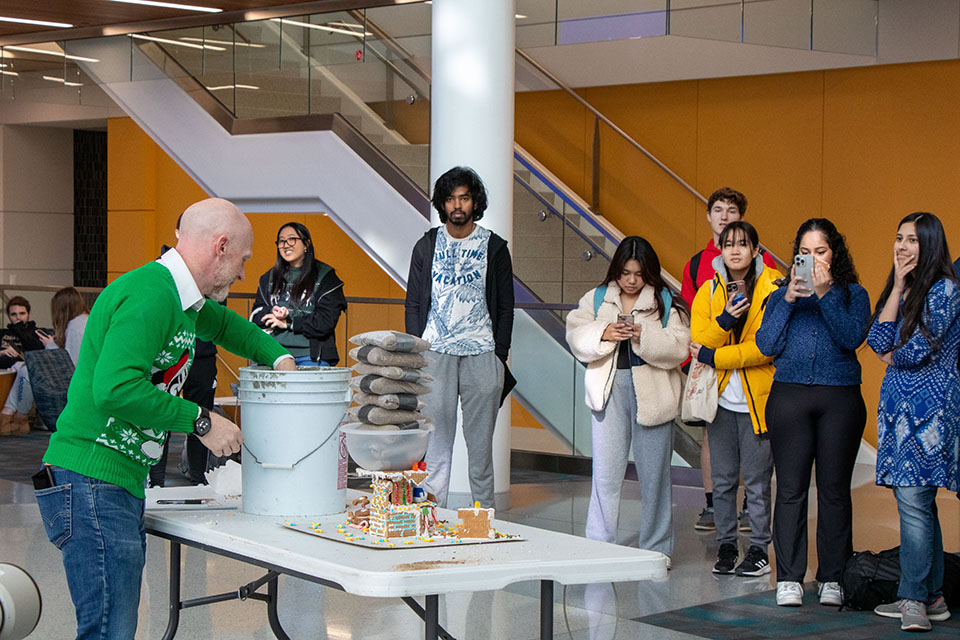Scott Sell, Ph.D., professor of biomedical engineering, adds weight to a gingerbread house built for SSE's December Innovation Challenge as students look on. Photo by Tyler Merkle. 