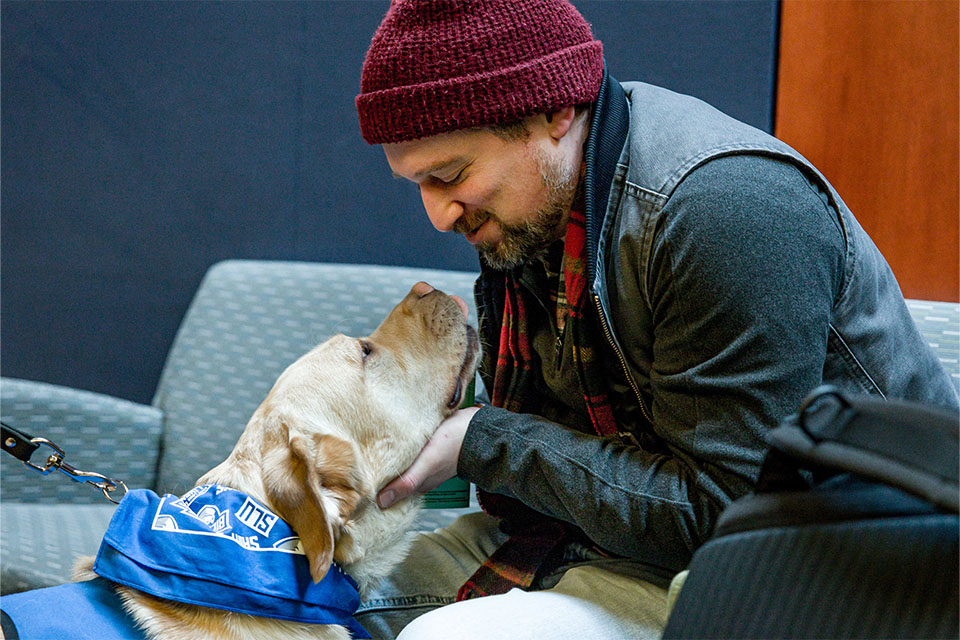 A student, seated, scratches Woody under the chin.