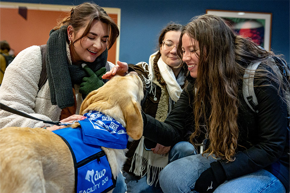 Three students smile as they pet Woody. 