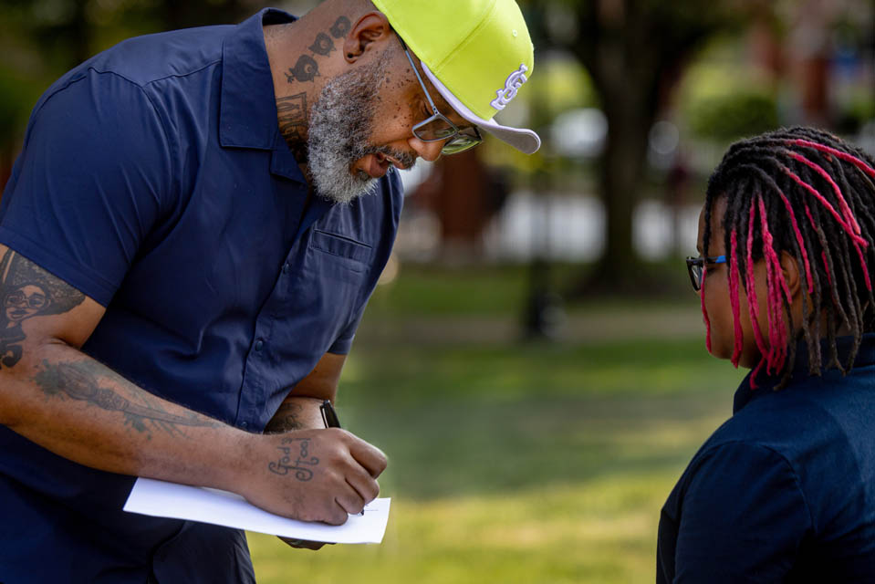 Artist Cbabi Bayoc signs an autograph for a young fan following the celebration for “The Legacy of Mill Creek,” an art installation surrounding the fountain at Grand and Lindell Blvds. The installation honors the vibrant historically Black community that lived in the former Mill Creek Valley neighborhood. Photo by Sarah Conroy. 