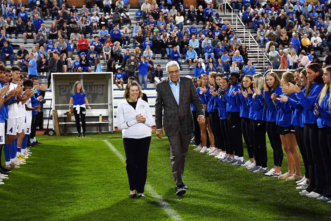 University President Fred P. Pestello, Ph.D, and First Lady Fran Pestello, Ph.D., walk on SLU's soccer field to be honored before the men's game.