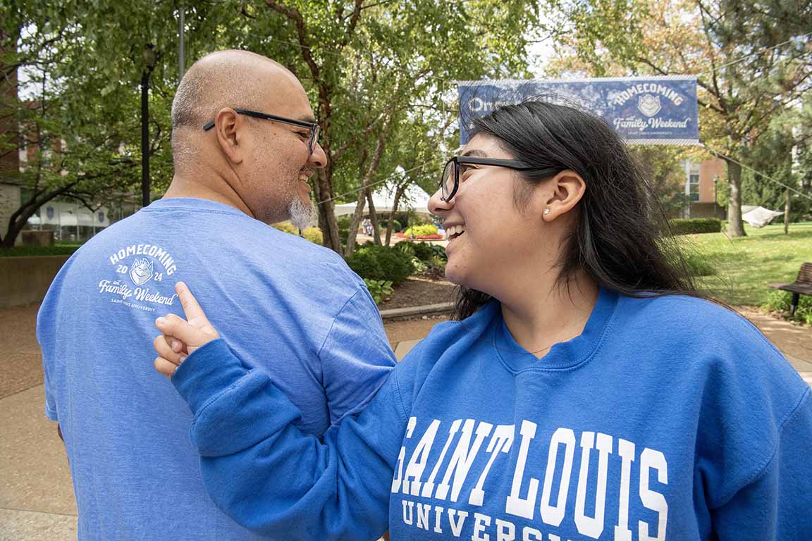 Attendees at 2024 Homecoming and Family Weekend stand on West Pine Mall in SLU gear pointing at each others' shirts.