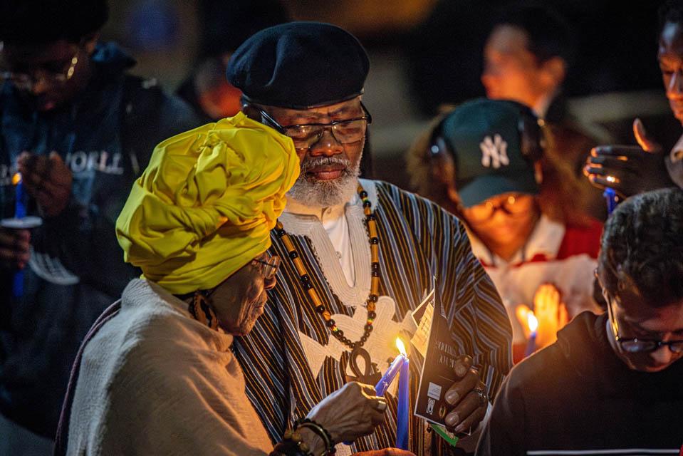 Descendant Mama Safiyah Chauvin, left, lights the candle of Baba Seba Amari Sneferu during the Lights of Remembrance Candlelight Vigil on Feb. 27, 2025. The event, organized and led by SLU graduate student Sam Hall in partnership with the Descendants of the St. Louis University Enslaved, formally honored the lives of enslaved individuals who helped build and sustain the University and other Jesuit missions in Missouri from 1823 to 1865. Photo by Sarah Conroy.  
