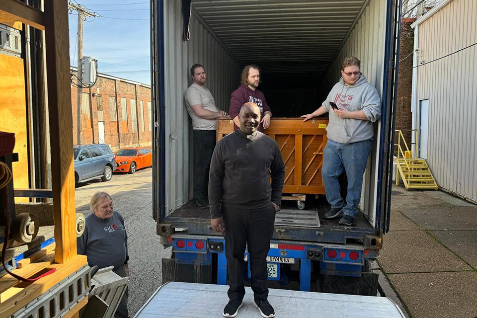 Fr. Thomas Sserwadda, a doctoral student at Saint Louis University, stands on a loading dock as a truck gets loaded with pianos. Submitted photo.