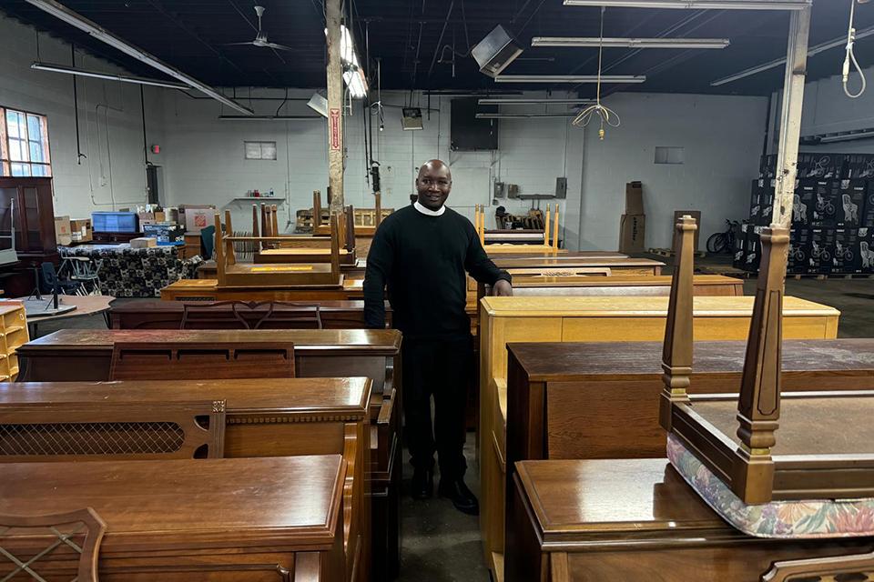 Fr. Thomas Sserwadda, a doctoral student at SLU, stands among pianos in a warehouse before they are shipped to Uganda. Submitted photo.