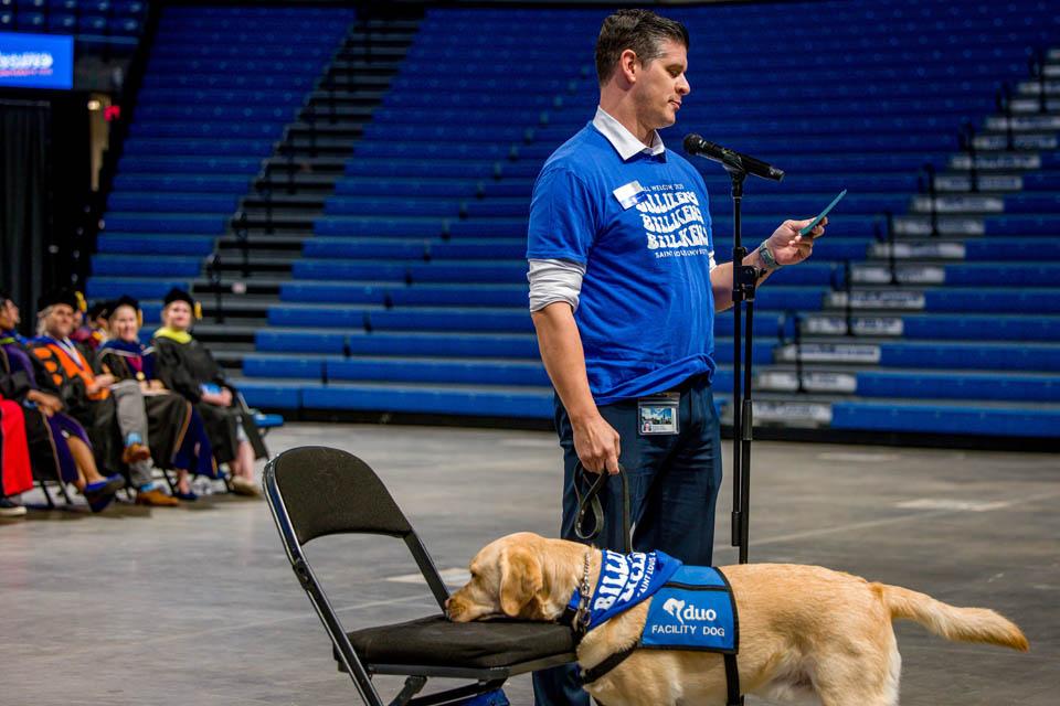 Matt Davis, chief of staff in the Provost’s office, and Duo Dog Woody speak during Convocation on Saturday, Aug. 16, 2025. Photo by Sarah Conroy. 