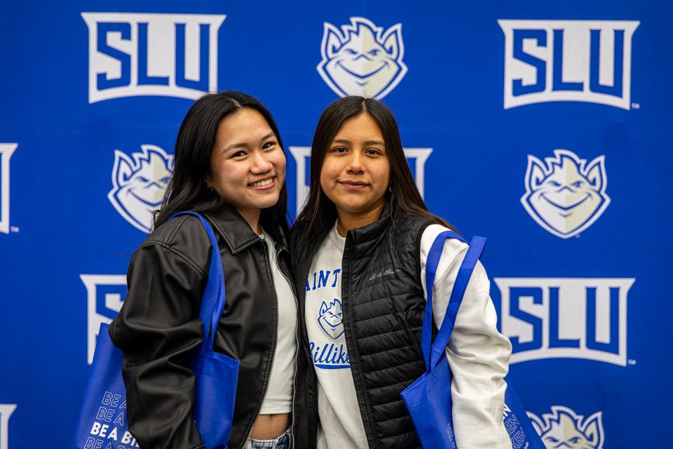 Two admitted students pose in front of the athletics backdrop.