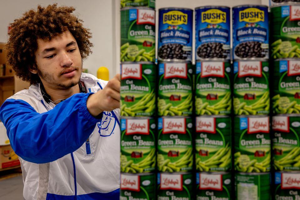 Aureous Ifabiyi-Chope, one of the two SLU designers for CANstruction, builds a practice bridge at Operation Food Search. Photo by Sarah Conroy. 