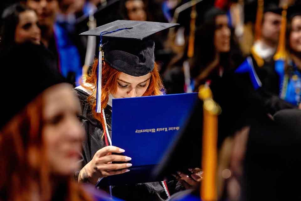 Paloma Ferreira de Oliveira looks at her diploma after receiving her Master of Arts from the College of Arts and Sciences during their precommencement ceremony on May 14, 2026. Photo by Sarah Conroy. 