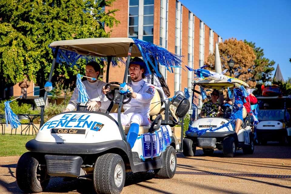 A line of decorated golf carts drive through campus.