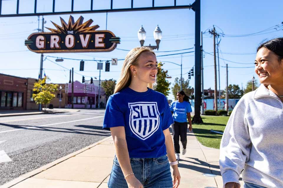 Female students walk on a sidewalk passing by a large sign that reads The Grove.