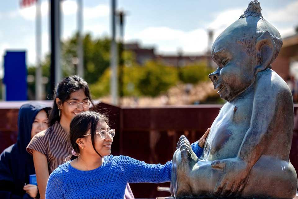Students line up at a campus statue to rub the belly.